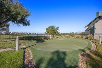 A putting green in front of a building with a fence